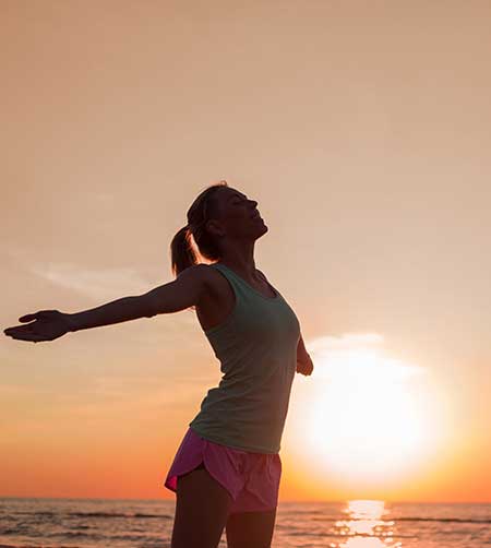 Woman with open arms in front of sunset