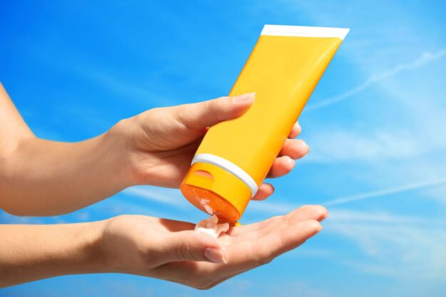 sunscreen shutterstock_531060736 Hands using sunscreen bottle.